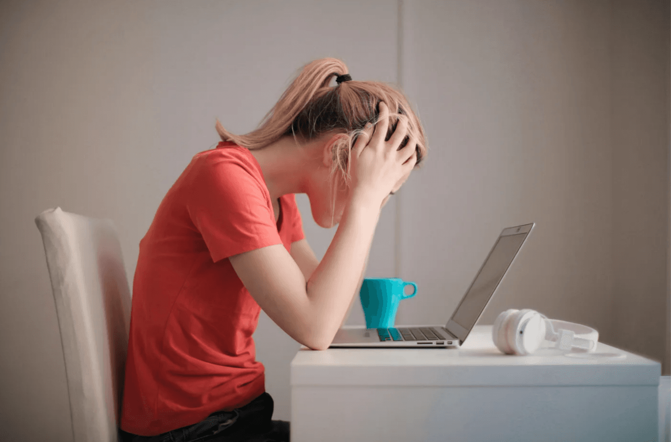 A tired female developer sitting at a desk with a laptop and coffee cup, holding her head in her hands.